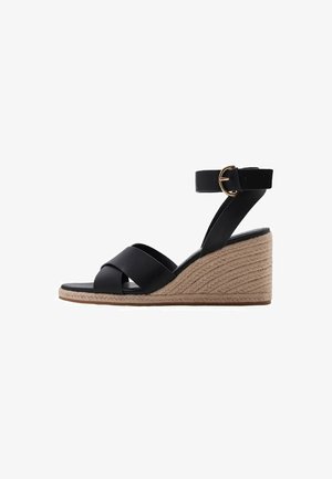 Sandales compensées noires avec des lanières croisées, dessus en simili cuir lisse, bride de cheville ajustable avec une boucle dorée, et plateforme en jute tressé.