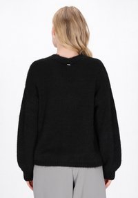 Czarny, puszysty sweter o szerokiej sylwetce, z prążkowanymi mankietami i subtelnym detalem na plecach. Miękka tekstura, stworzony do codziennego noszenia.