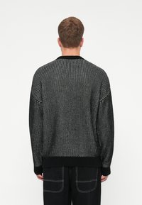 Maglione lavorato a maglia in bianco e nero con vestibilità comoda, caratterizzato da un collo a costine e motivi testurizzati su tutta la superficie. Mostrato da dietro.