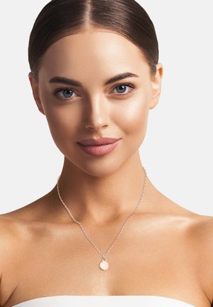 Roségold-Halskette mit einem runden Anhänger an einer dünnen Kette, getragen von einem Modell vor einem neutralen Hintergrund, der die Textur des Anhängers zur Schau stellt.