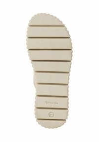 Ljusbeige gummisula med horisontella ribbor, vågiga kanter och varumärkeslogotyp. Ytan verkar något strukturerad för grepp.