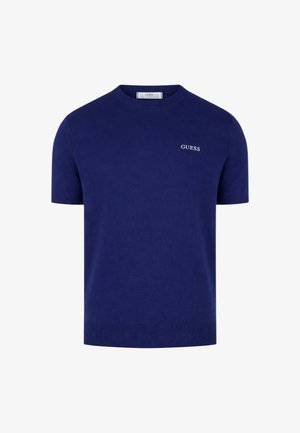 Chemise tricotée bleu marine à manches courtes avec ourlet et poignets côtelés, arborant un petit logo blanc "GUESS" sur la poitrine gauche.