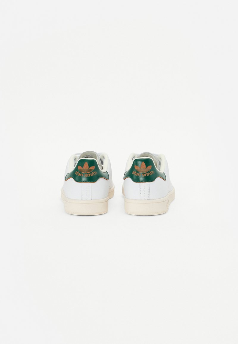 Baskets blanches en cuir avec des accents verts, dotées d'une languette de talon texturée et d'un logo "Stan Smith" doré, ainsi qu'une semelle en caoutchouc clair.