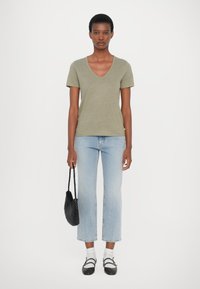 Olivgrön v-ringad t-shirt, kombinerad med ljusblå raka jeans och svart vävd väska. Vita strumpor och svarta remsandaler fulländar looken.
