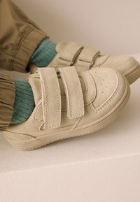 Beiget mokkanahkaiset kengät, joissa on kaksois-tarranauhat, rei'itetty varvasosa ja kumipohjat. Yhdistetty turkoosiin ribbineulossukkiin ja vaaleanruskeisiin housuihin.