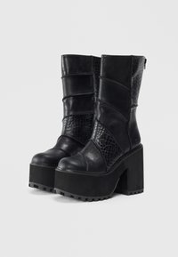 Botas de plataforma de cuero negro con tacones gruesos, acentos de patrón de cocodrilo y cierre de cremallera en la parte trasera.