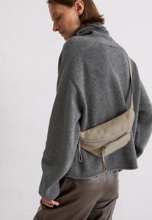 Beige nylon crossbody bag with two zippered compartments, worn over a gray knit sweater. The bag features a smooth texture and adjustable strap.