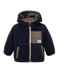 Marineblauw fleecejack met een capuchon, voorzien van een beige borstzak, zijzakken en een volledige ritssluiting aan de voorkant. Zachte textuur en oversized ontwerp.