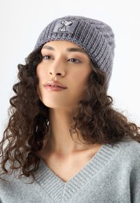 Grijze gebreide beanie met een gestructureerd patroon en een zwart-wit Snoopy-patch aan de voorkant. Zacht, warm materiaal met een comfortabele pasvorm.