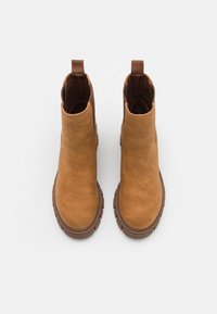 Stivali alla caviglia in pelle marrone con una texture liscia, punta arrotondata e un cappio sul retro. Suola in gomma con dettagli di presa.