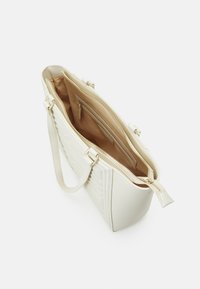 Sac à main en simili cuir blanc avec texture rayée, fermeture éclair et double poignées. L'intérieur est garni de beige et comporte plusieurs compartiments.