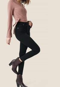 Rosa ribbad omslagstopp, svarta högmidjade jeans och burgundyröda klackade anklarstövlar med en texturerad yta och sidogångjärn.