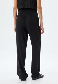 Zwarte, wijde broek met een ontspannen pasvorm, met een gladde textuur en geplooide achterkant. Minimalistische stijl zonder zichtbare patronen.