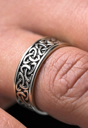 Keltisk mønster ring med sammenflettede sorte metalldesign på en polert sølvring. Detaljert, teksturert overflate med glatte kanter.