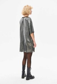 Robe argentée chatoyante avec une coupe ample, des manches courtes et des fentes sur les côtés, associée à des bottes noires à lacets montantes et des collants transparents.
