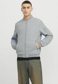 Helle graue Bomberjacke mit einem Reißverschluss vorne, gerippten Bündchen und Saum sowie seitlichen Taschen. Weiche Textur mit minimalistischem Design.