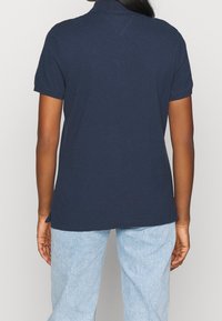 Mörkblå pikétröja med korta ärmar, platt krage och rak passform, tillverkad av mjukt bomullsmaterial. Bakifrån med inga synliga detaljer.