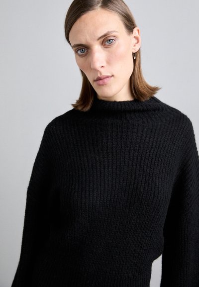 Pulover negru cu nervuri, cu un design la gât înalt, cu o textură moale și o croială lejeră, prezentat pe un fundal neutru.
