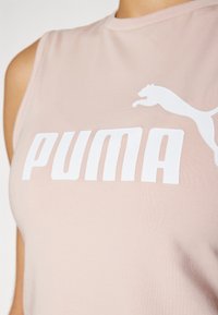Svijetloružičasti top bez rukava s glatkom teksturom, s velikim bijelim logotipom "PUMA" i grafikom skakačke mačke sa strane.