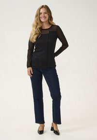 Juodas ilgų rankovių marškinėlis su permatomomis detalėmis ir vertikaliomis riebėmis, derinamas su tamsiai mėlynais tiesiais džinsais ir juodais aukštakulniais batais.