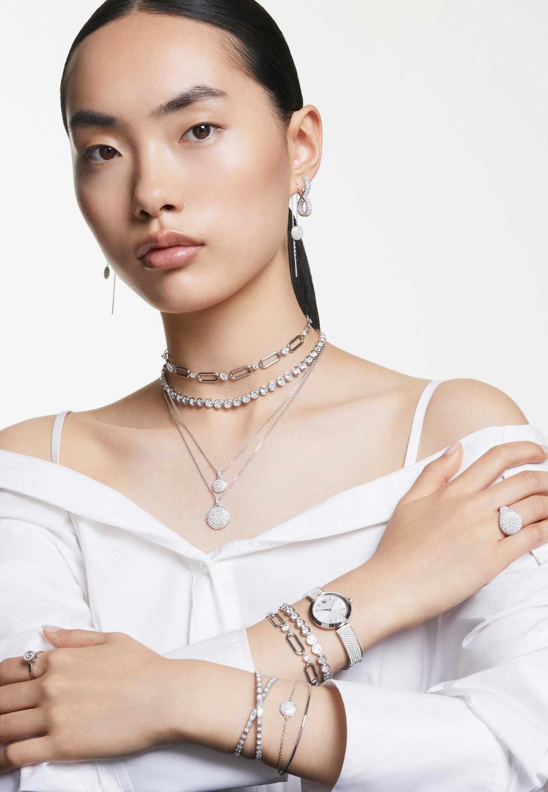 Srebrna biżuteria, w tym warstwowe naszyjniki, kolczyki, zegarek oraz pierścionki o okrągłych i owalnych kształtach, z gładkimi i teksturowanymi powierzchniami.