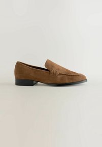 Mocassin en daim marron avec petit talon noir, détail avant cousu et design de style mocassin sur un fond clair uni.