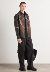 Chemise à boutons ornée d'un motif abstrait sombre ; associée à un pantalon cargo noir et des baskets noires élégantes. Les accessoires comprennent un grand sac noir.