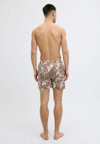 Pantaloni da nuoto marroni con un leggero motivo floreale, vita elasticizzata e taglio al di sopra del ginocchio, mostrati da dietro su un modello con la pelle nuda.