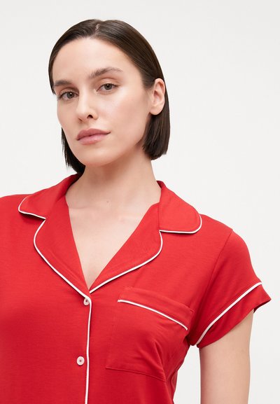 Red short-sleeve pajama top in soft fabric, featuring a button-down front, white piping along the collar, and a small pocket on the left chest.