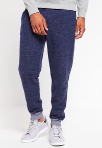 Marineblaue Fleece-Jogginghosen mit weicher Textur, elastischen Bündchen und entspannter Passform, kombiniert mit hellgrauen Sneakers mit perforiertem Design.