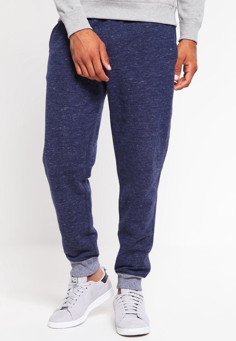 Marineblaue Fleece-Jogginghosen mit weicher Textur, elastischen Bündchen und entspannter Passform, kombiniert mit hellgrauen Sneakers mit perforiertem Design.