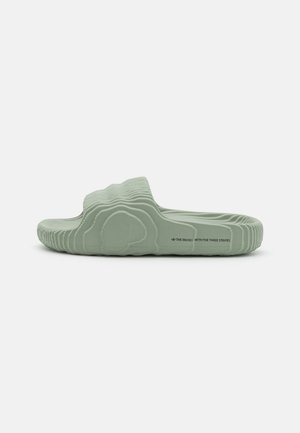 Une sandale slide verte unique avec un motif ondulé texturé et le texte « The Brand with the Three Stripes » sur le côté de la semelle.