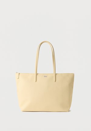 Beige tote bag with double handles, zipper closure, and a small silver logo centered near the top.