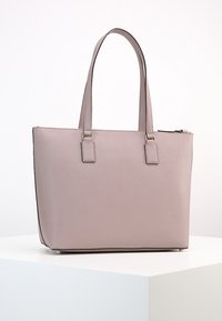 Vaaleanpunainen laukku, jossa on jämäkkä muotoilu, kaksi pitkää kantohihnaa, teksturoitu pinta ja vetoketjukohta. Varustettu kultaisilla koristeosilla.