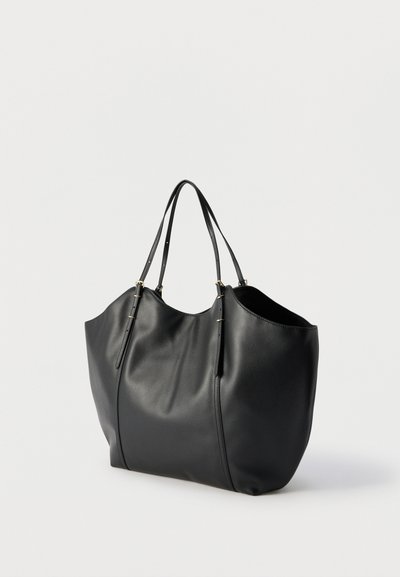Sac fourre-tout en cuir noir avec doubles anses d'épaule et détails de boucles dorées, présenté sur un fond clair uni.