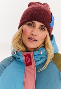 Barevná péřová bunda s modrými, růžovými a zelenými panely. Měkká fleecová vínová čepice s modrou visačkou. Výrazné švy a zipy.