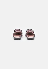 Sandali neri slip-on con una parte superiore in tessuto decorato che presenta colori ondulati. La suola è piatta e testurizzata, con un sottopiede rosa.