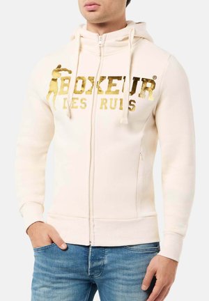 Hellbeige Zip-Up-Hoodie aus einer weichen Baumwollmischung, mit goldenen Blockbuchstaben und einer Kängurutasche. Mit Kordelzugkapuze und gerippten Ärmelbündchen.