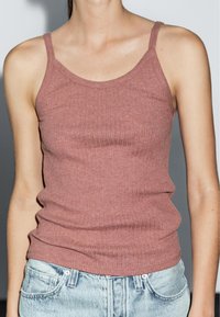 Top a canotta a coste color rosa polveroso, realizzato in tessuto elasticizzato. Presenta spalline sottili e una forma aderente, abbinato a jeans in denim chiaro.