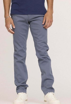 Pantalon en coton bleu clair avec une coupe slim, design à cinq poches et coutures contrastées, associé à des baskets blanches.