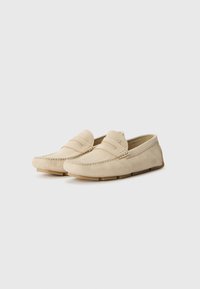 Beige suede loafers with stitched detailing, low profile, and rubber soles, featuring dual straps across the instep for added texture.