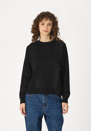 Black sweater with lace detailing on the front, round neck, and long sleeves. Paired with blue denim jeans. Soft fabric with a relaxed fit.