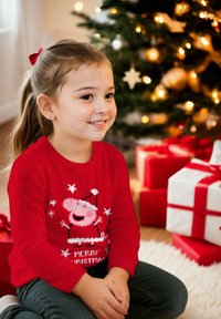 Maglione rosso lavorato a maglia con un personaggio dei cartoni animati, un maialino rosa in un cappello da Babbo Natale, con fiocchi di neve bianchi e la scritta "Buon Natale", abbinato a jeans scuri.