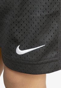 Svart sportslige shorts laget av nettstoff med små perforeringer. Har en hvit Nike-logo sydd på kanten. Glatt tekstur.