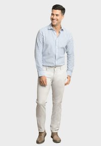 Camisa de hombre de botones con rayas verticales en azul y blanco, combinada con pantalones beige y zapatos marrones. Textura suave, cuello clásico.