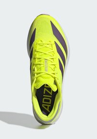 Baskets de sport jaune vif avec des accents violets, tige en mesh et surface texturée. Présente des lacets et un col rembourré pour le confort.