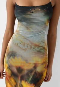 Šaty bodycon s květinovým vzorem v odstínech zelené a žluté, vyrobené z elastického materiálu, s tenkými špagetovými ramínky a přiléhavým siluetou.