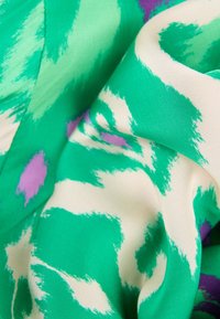 Zielono-i-kremowy materiał z fakturowanym wzorem ikat, z odważnymi zielonymi pociągnięciami pędzla i akcentami liliowymi, tworzącym abstrakcyjny design.