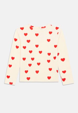 Chemise crème à manches longues avec motifs de cœurs rouges dispersés, encolure ronde et fermeture à boutons dans le dos.