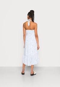 Vestido floral azul claro com corpete ajustado e saia rodada, apresentando um laço no pescoço halter. Feito de um tecido leve e texturizado.